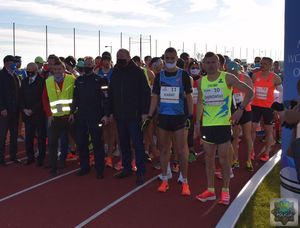 biegacze ustawieni na linii startu na czerwonej bieżni lekkoatletycznej. Po środku przedstawiciele władz - organizatorzy mistrzostw, po  środku umundurowany policjant - Komendant Powiatowy Policji w Oleśnie - insp. Tomasz Kubicki