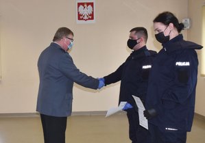 Pierwszy  Zastępca Komendanta Powiatowego Policji w Oleśnie - mł.insp. Waldemar Popczyk wręcza rozkazy o przyjęciu do służby nowo przyjętym funkcjonariuszom - ściska dłoń nowego policjanta. Policjantka trzyma w rękach rozkaz . W tle na ścianie godło Rzeczypospolitej Polski.