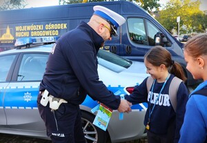 zdjęcie kolorowe: policjanci rozdają dzieciom kaski i elementy odblaskowe